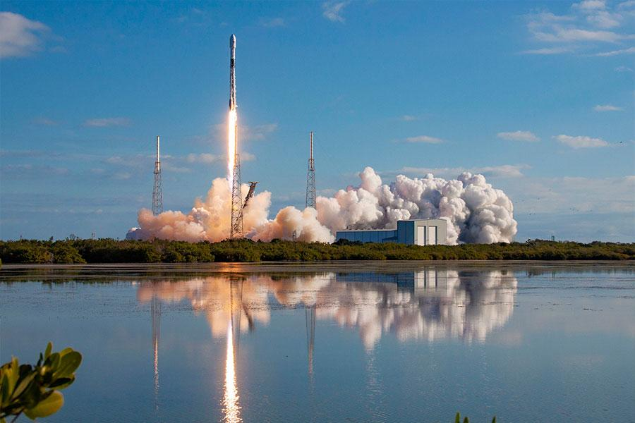 Rocket launching into a clear blue sky with its reflection in calm water
